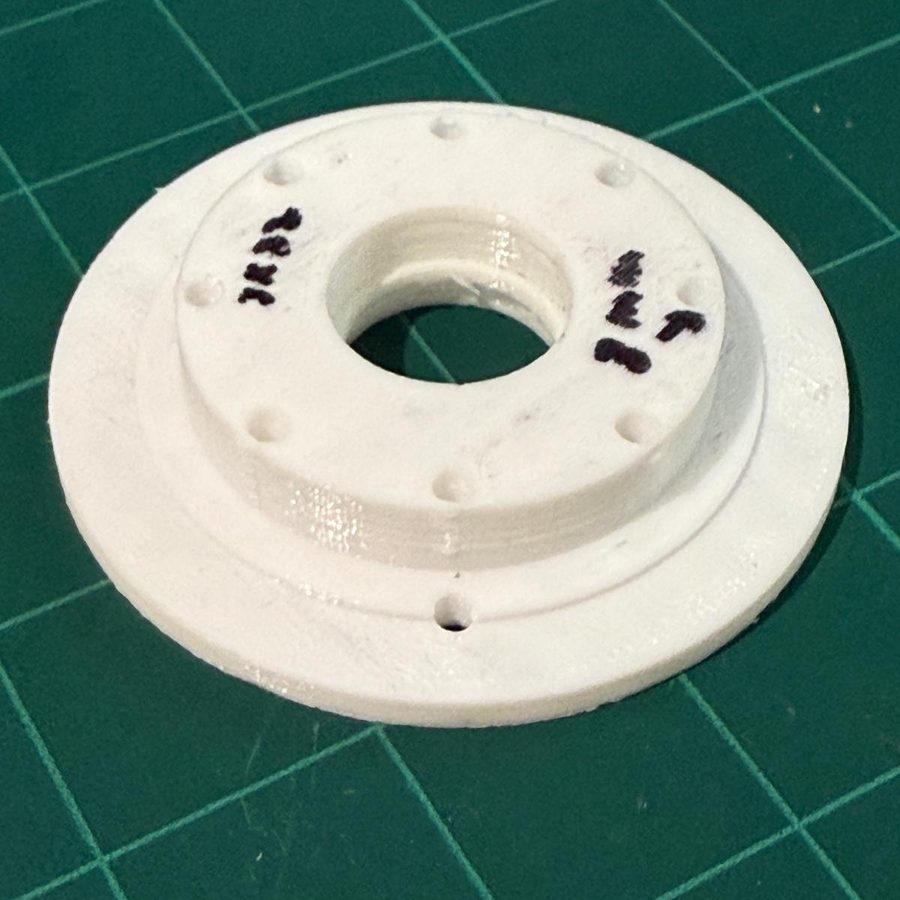 White circular bearing plate with a stepped profile, central bore, ring of holes around it, and hand-drawn pen marks on the face