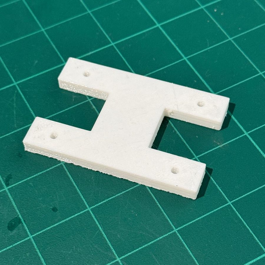Flat white plate in an H shape with two holes at each end