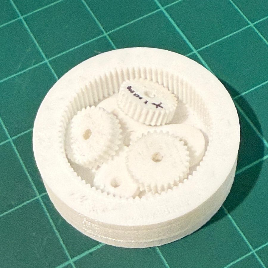3D printed planetary gear set with an outer ring gear, three planet gears and a central sun gear, printed fully assembled in white filament on a green cutting mat