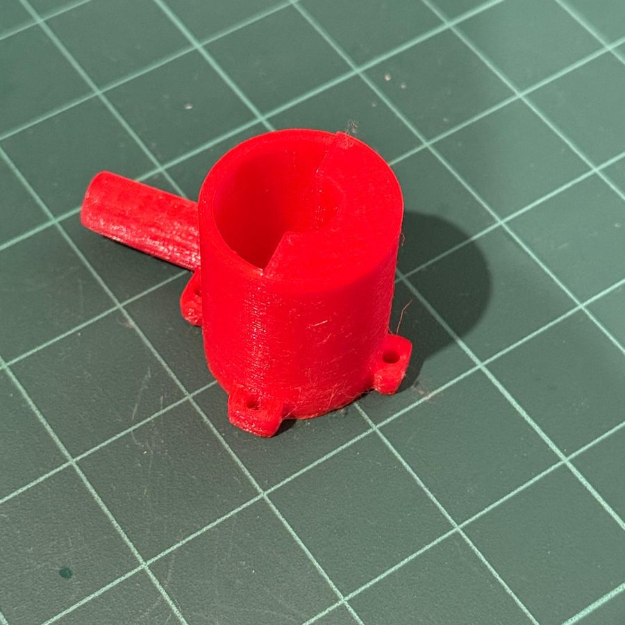 Red cylindrical housing with an open bore, a side outlet spout and two flanged feet with mounting holes